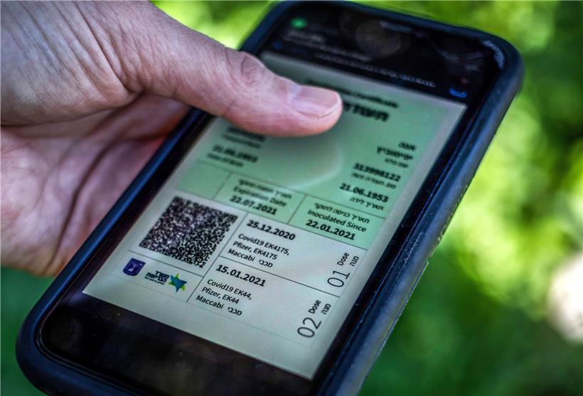 Ein israelischer Mann hält ein Smartphone in der Hand, auf dem der sogenannte „grüne Pass“ abgebildet ist, ein Zertifikat, das an Menschen ausgegeben wird, die vollständig geimpft sind
