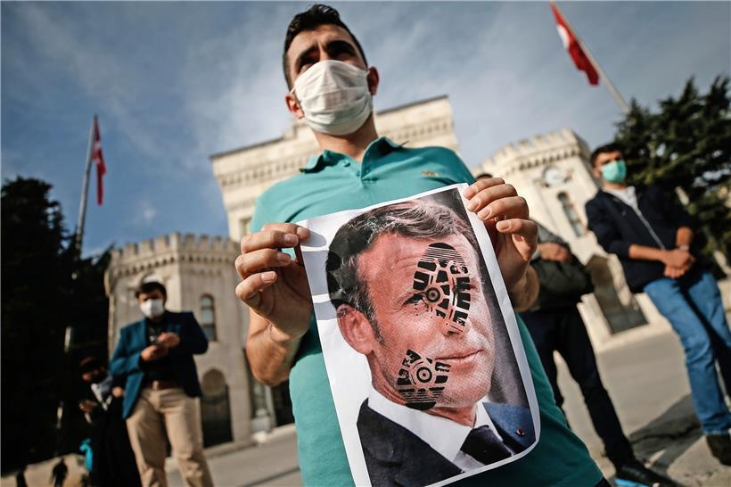 Ein junger Mann in Istanbul hält ein mit einem Schuhabdruck versehenes Foto von Frankreichs Präsident Emmanuel Macron in die Kamera

