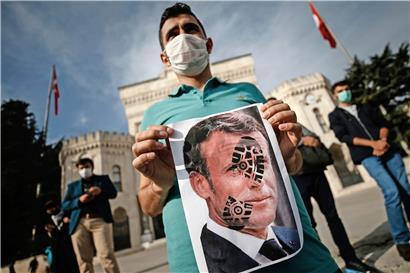 Ein junger Mann in Istanbul hält ein mit einem Schuhabdruck versehenes Foto von Frankreichs Präsident Emmanuel Macron in die Kamera
