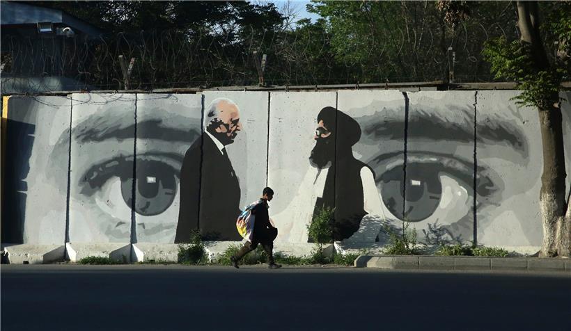 Ein kleiner Junge trägt einen Sack mit Waren auf seinem Rücken und geht an einer Wand vorbei, auf der Zalmay Khalilzad (l), Friedensgesandter aus Washington, und Mullah Abdul Ghani Baradar, Leiter der Taliban-Delegation, abgebildet sind
