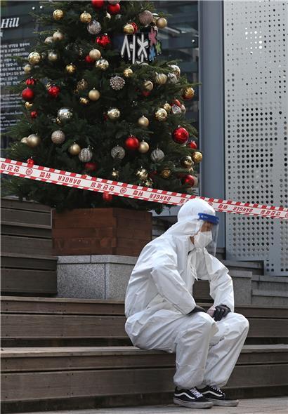 Ein medizinischer Arbeiter in Schutzkleidung sitzt in einer behelfsmäßigen Klinik in Seoul bei einem Weihnachtsbaum und macht eine Pause
