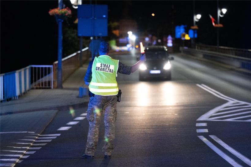 Ein polnischer Grenzschützer steht auf der polnischen Seite hinter der Stadtbrücke von Görlitz und winkt ein Fahrzeug zur Kontrolle raus
