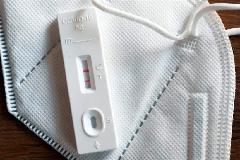Ein positiver Corona-Selbsttest und eine FFP2-Schutzmaske liegen auf einem Tisch 
