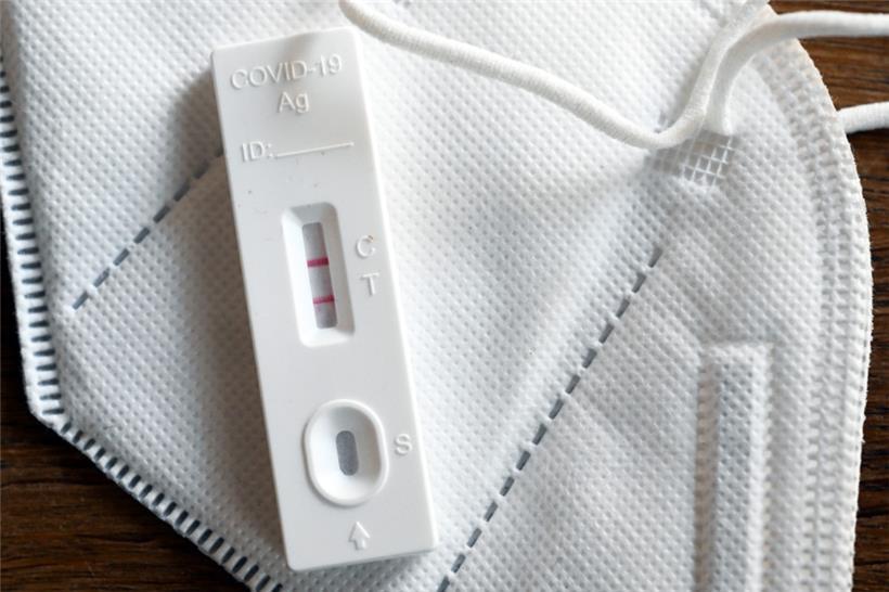 Ein positiver Corona-Selbsttest und eine FFP2-Schutzmaske liegen auf einem Tisch 
