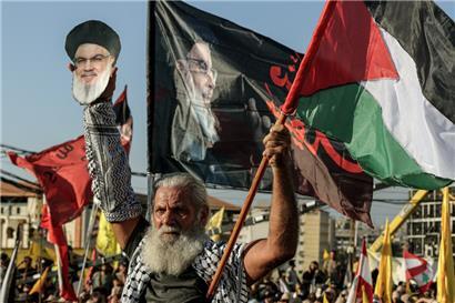 Ein pro-iranischer Hisbollah-Anhänger hält ein ausgeschnittenes Porträt des ermordeten Hisbollah-Chefs Hassan Nasrallah und eine palästinensische Fahne während einer Zeremonie an Nasrallahs Grab anlässlich des ersten Jahrestages seiner Ermordung durch einen massiven israelischen Luftangriff hoch
