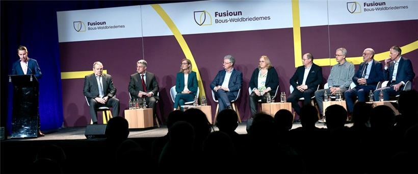 Ein prominent besetztes Podium bei der Infoveranstaltung über die geplante Fusion von Bous und Waldbredimus: Carlo Kütten, Bürgermeister von Bous, Thomas Wolter, Bürgermeister von Waldbredimus, LSAP-Innenministerin Taina Bofferding, Syvicol-Präsident und Bürgermeister von Clerf, Emile Eicher (CSV), daneben Vertreter der beiden Schöffenräte
