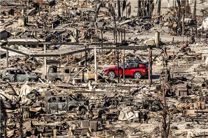 Ein rotes Auto fährt an Häusern und Fahrzeugen vorbei, die durch das Palisades-Feuer in den Pacific Palisades Bowl Mobile Estates zerstört wurden
