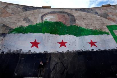 Ein syrischer Junge steht unter einem riesigen Porträt des verstorbenen syrischen Präsidenten Al-Assad, übermalt mit den Farben der sogenannten „revolutionären“ Flagge
