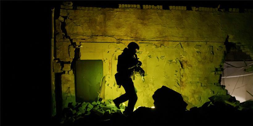 Ein ukrainischer Spezialpolizist patrouilliert neben einem zerstörten Gebäude während der nächtlichen Ausgangssperre
