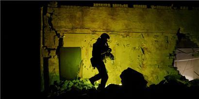 Ein ukrainischer Spezialpolizist patrouilliert neben einem zerstörten Gebäude während der nächtlichen Ausgangssperre
