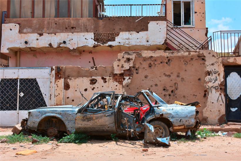 Ein zerstörtes Auto steht vor einem Haus voller Einschüsse. Im Sudan herrscht seit fast 16 Monaten ein blutiger Machtkampf.
