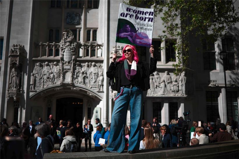 Eine Aktivistin hält vor dem Obersten Gerichtshof in London ein Plakat mit der Aufschrift „Frauen werden geboren, sie sind nicht irgendein Kerl mit einem Formular“ hoch
