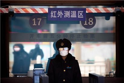 Eine Bahnhofsangestellte trägt einen Mundschutz und eine Schutzbrille, während sie darauf wartet, die Fahrkarten der Passagiere am Bahnhof von Peking zu kontrollieren

