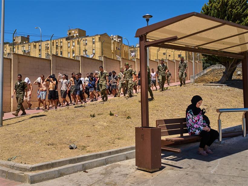 Eine Einwohnerin von Ceuta sitzt an einer Bushaltestelle, während Migranten, die nach Spanien eingereist sind, von spanischen Soldaten in Richtung der spanisch-marokkanischen Grenze eskortiert werden