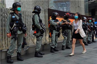 Eine Frau, die wegen der Corona-Pandemie einen Mundschutz trägt, geht an Bereitschaftspolizisten im Central Disctrict vorbei. Die Hongkonger Polizei steht auch am zweiten Tag der Debatte über ein umstrittenes Gesetz gegen den Missbrauch der chinesischen Nationalhymne Wache. 
