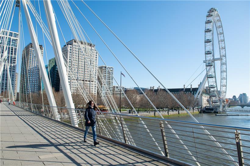 Eine Frau geht über die Golden Jubilee Fußgängerbrücke im Zentrum Londons. 
