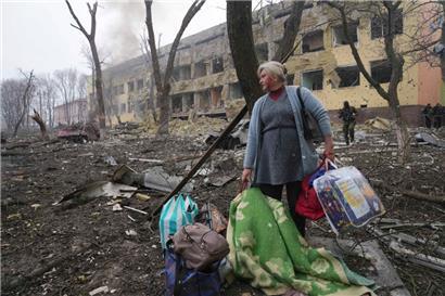 Eine Frau steht mit ihrem Gepäck vor einer durch einen Angriff beschädigten Geburtsklinik in Mariupol
