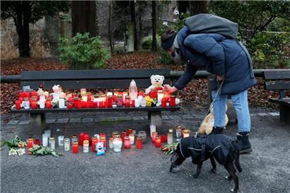Eine Frau stellt eine Trauerkerze neben Blumen und Kuscheltieren nach dem tödlichen Angriff in einem Park am Tatort auf einer Bank ab
