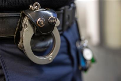 Eine Handschelle hängt am Gürtel eines Polizisten
