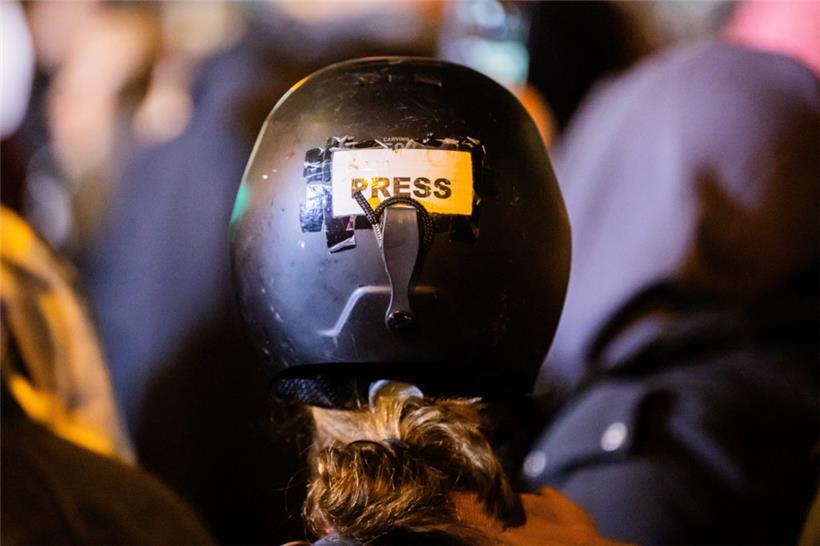 Eine Journalistin macht ihre Rolle auf einer Demonstration durch einen Aufkleber auf ihrem Helm deutlich
