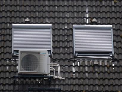 Eine Klimaanlage ist am Dach eines Wohngebäudes unter Dachfenstern zu sehen