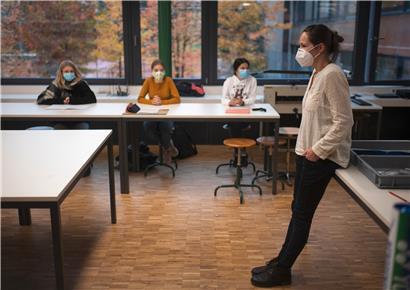 Eine Lehrerin mit einer Schutzmaske steht vor einer Schulklasse, in der die Schülerinnen einen Mund-Nasen-Schutz tragen. Welche Rolle spielen Erwachsene bei der Übertragung von Covid-19 in den Schulen?
