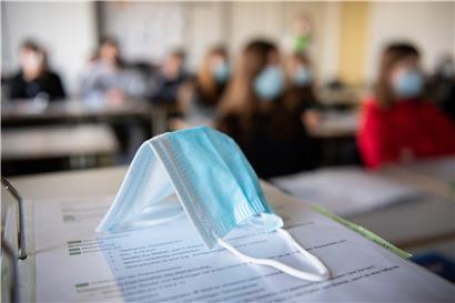 Eine Maske liegt auf einem Arbeitsordner in einer Schule. Zwar meldet das Bildungsministerium keine weiteren Infektionsketten, dennoch stieg die Zahl positiv getesteter Schüler und Lehrer weiter.

