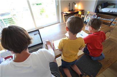 Eine Mutter arbeitet zu Hause an einem Laptop, während ihre Kinder neben ihr malen
