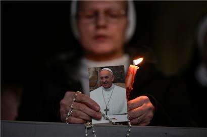 Eine Nonne hält eine Kerze und ein Bild von Papst Franziskus während eines Rosenkranzgebets für seine Gesundheit auf dem Petersplatz im Vatikan
