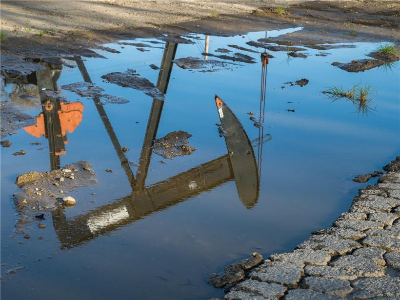 Öl-Pumpe spiegelt sich klar in einer Pfütze auf dem Industriegelände bei Sonnenuntergang