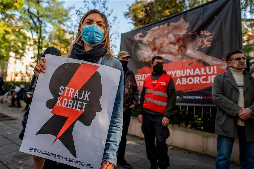 Eine Pro-Choice-Aktivistin demonstriert vor dem Verfassungsgericht in Warschau für ein Recht auf Abtreibung – auf dem Plakat steht „Frauenstreik“. Im Hintergrund ein Plakat der Abtreibungsgegner.
