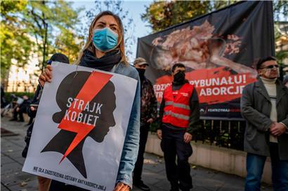 Eine Pro-Choice-Aktivistin demonstriert vor dem Verfassungsgericht in Warschau für ein Recht auf Abtreibung – auf dem Plakat steht „Frauenstreik“. Im Hintergrund ein Plakat der Abtreibungsgegner.
