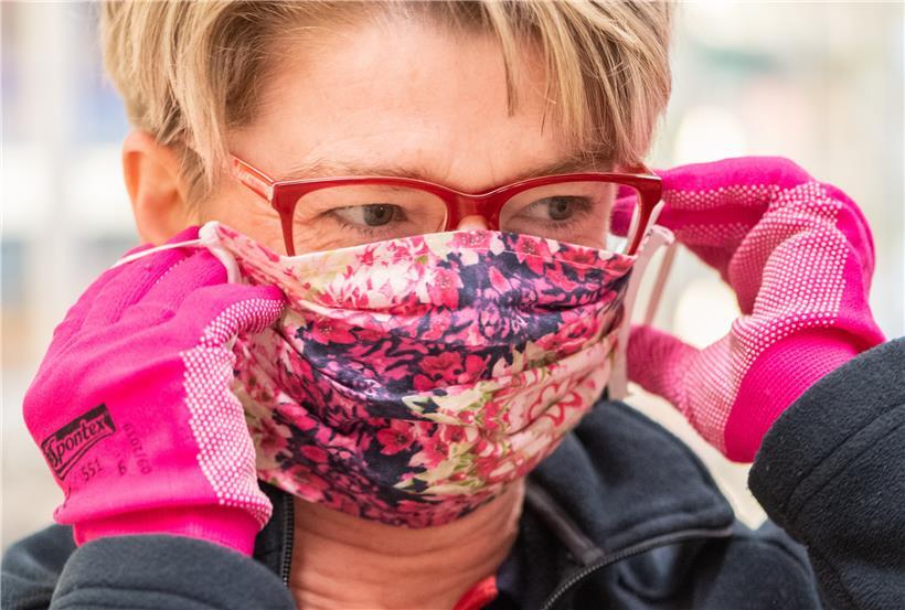 Eine Supermarktverkäuferin zieht eine bunt bedruckte Schutzmaske an

