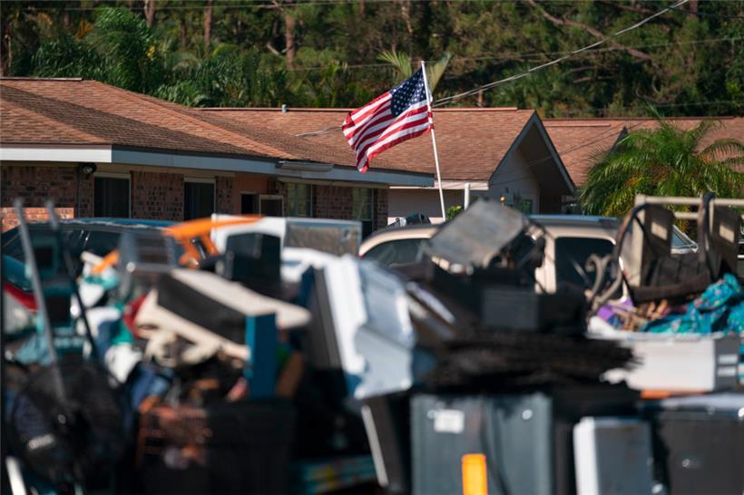 Eine amerikanische Flagge hinter Stapeln von überschwemmungsgeschädigtem Eigentum in Bonita Springs, Florida
