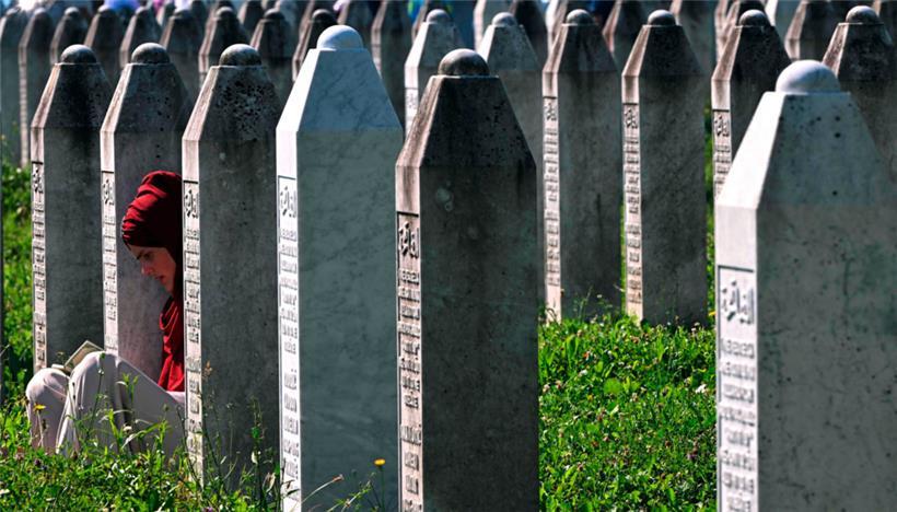 Eine bosnische Muslimin sitzt zwischen Grabsteinen und liest auf dem Gedenkfriedhof des Dorfes Potocari in der Nähe der ostbosnischen Stadt Srebrenica
