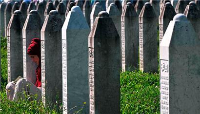 Eine bosnische Muslimin sitzt zwischen Grabsteinen und liest auf dem Gedenkfriedhof des Dorfes Potocari in der Nähe der ostbosnischen Stadt Srebrenica
