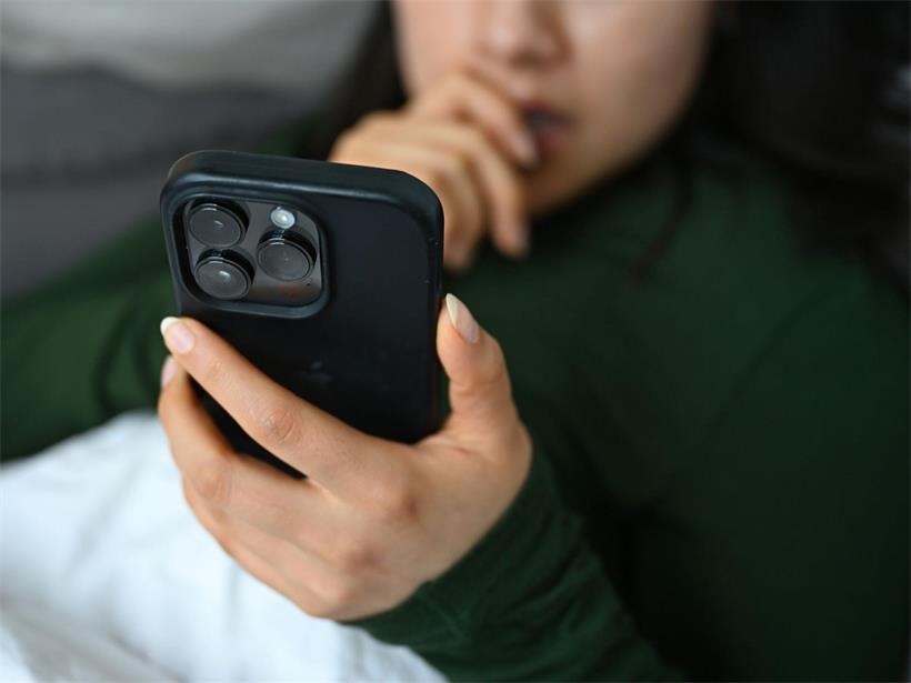 Eine junge Frau liegt mit ihrem Handy auf der Couch und blickt auf das Display