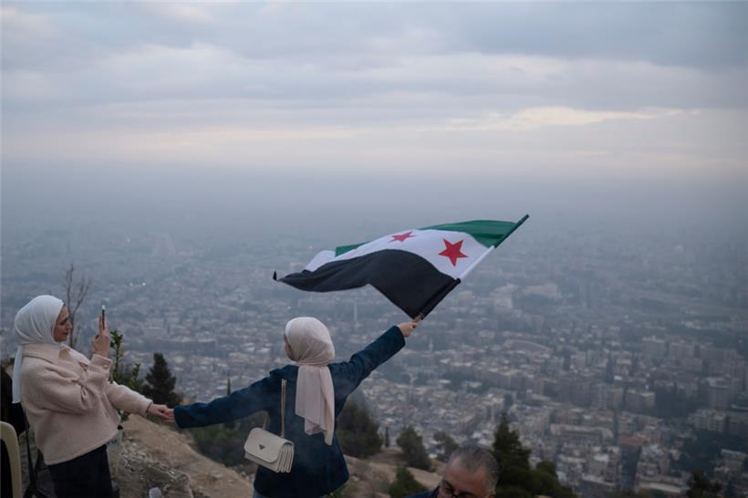 Eine junge Frau posiert für ein Foto mit einer Flagge der syrischen Opposition an einem Aussichtspunkt auf dem Berg Qasiyun oberhalb der Stadt Damaskus
