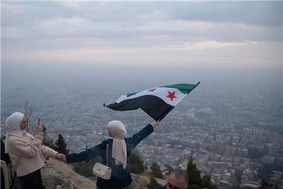 Eine junge Frau posiert für ein Foto mit einer Flagge der syrischen Opposition an einem Aussichtspunkt auf dem Berg Qasiyun oberhalb der Stadt Damaskus
