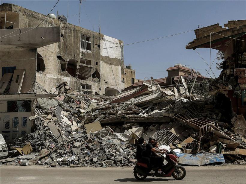 Libanesische Familie auf Motorrad fährt an zerstörten Gebäuden in Tyrus nach israelischen Luftangriffen vorbei