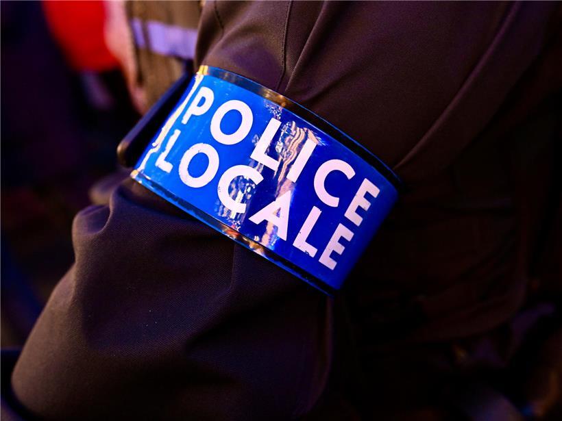 Dorfpolizist mit blauer Armbinde steht lächelnd vor ländlichem Hintergrund, Symbol für Sicherheit im Dorf