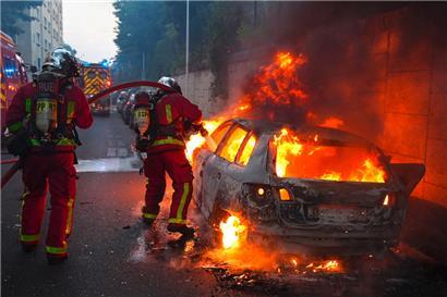 Feuerwehrleute löschen ein brennendes Auto am Rande einer Demonstration in Nanterre, westlich von Paris, am 27. Juni 2023, nachdem die französische Polizei einen Teenager erschossen hatte, der sich geweigert hatte, für eine Verkehrskontrolle in der Stadt anzuhalten
