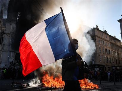 Frankreich, Marseille: Ein Demonstrant, der eine französische Nationalflagge schwenkt, geht während Zusammenstößen vor Beginn einer Demonstration gegen die „hohen Lebenshaltungskosten“ an einem Feuer vorbei. Die Aktion ist Teil eines landesweiten Mobilisierungsaufrufs, der verschiedene Gruppen zusammenbringt