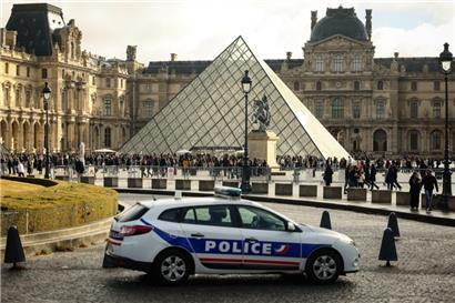 Frankreich, Paris: Ein Polizeiauto parkt im Hof des Louvre während Besucher vor der Glaspyramide in einer Schlange stehen.

