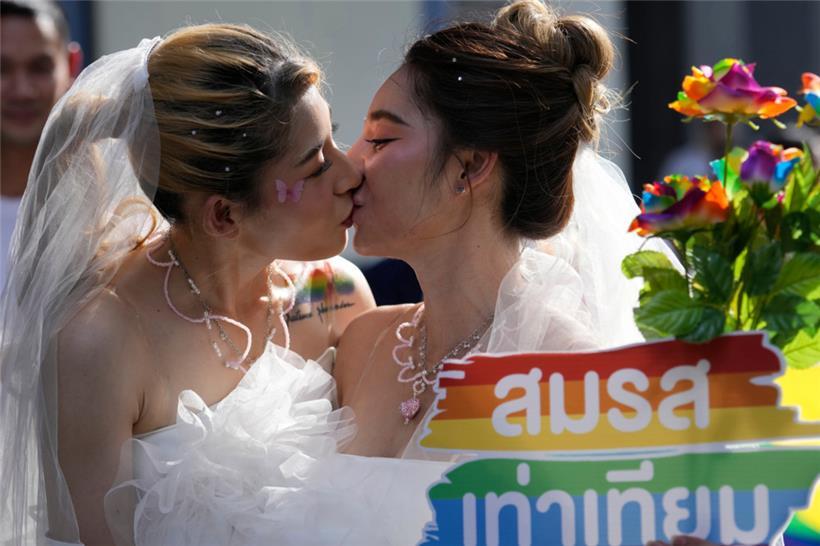 Frauen küssen sich während einer Pride-Parade in Bangkok, während sie ein Plakat zur Unterstützung der Ehegleichheit halten. Ab dem 23. Januar ist in Thailand die „Ehe für alle“ erlaubt. 
