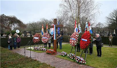 Gedenkzeremonie am historischen Hinzerter Kreuz mit Teilnehmern und Blumenarrangements bei sonnigem Wetter