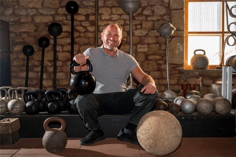 Georges Christen hockt in seiner Trainingsscheune vor historischen Hanteln und Gewichten
