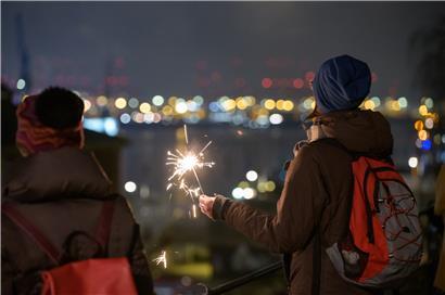 Große Feiern gab es dieses Silvester nicht. Eine Frau hat kurz nach dem Jahreswechsel eine Wunderkerze gezündet und schaut auf das Hafenpanorama von Hamburg.  
