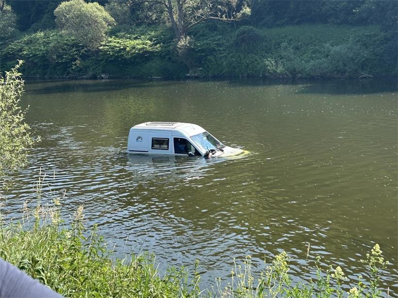 Helfer ziehen mit Traktor und Seilwinde ein Auto aus einem Fluss bei einer Bergungsaktion