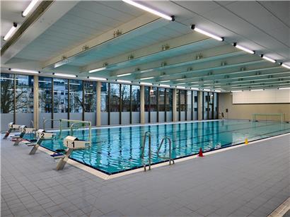 Leeres Hallenbad in Düdelingen mit stiller, blauer Wasseroberfläche und leeren Schwimmbahnen